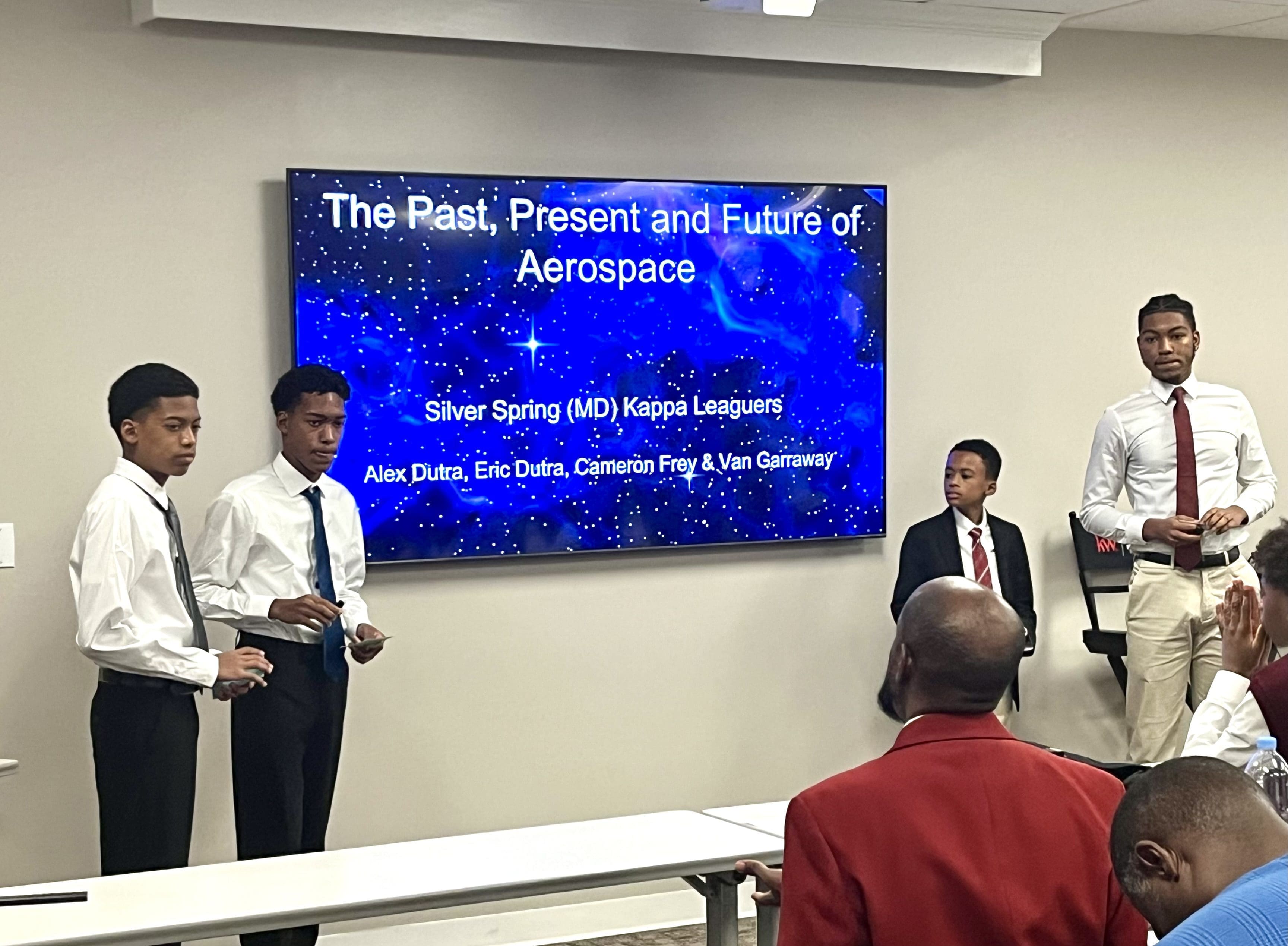 MKYF The Innovation Team, comprised of young men, is standing in front of a large screen to receive congratulations for their Guide Right efforts.