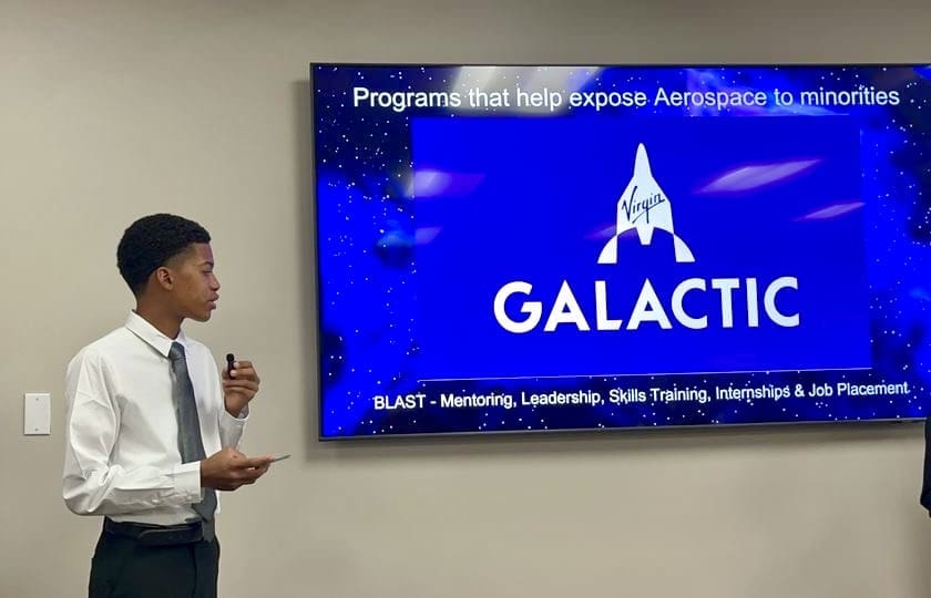MKYF Two young men from the Innovation Team standing in front of a tv with the word galactic on it.