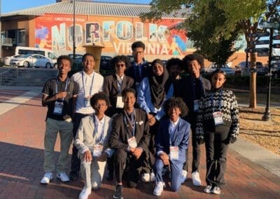 MKYF Group of smiling people posing in front of a "greetings from norfolk virginia" mural.