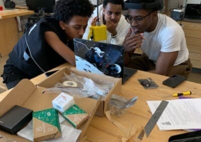 MKYF Three individuals engaged in a collaborative project at a workbench with various tools and components.