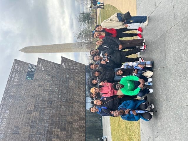 MKYF Group of people posing for a photo in front of the national museum of african american history and culture with the washington monument in the background.