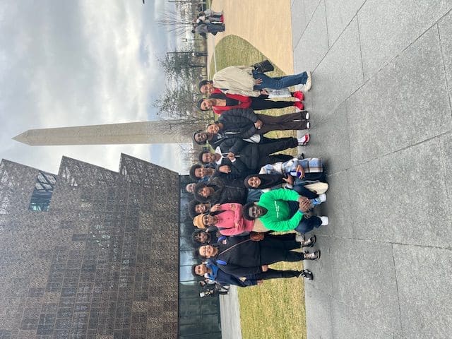 MKYF Group of people posing for a photo in front of the national museum of african american history and culture with the washington monument in the background.