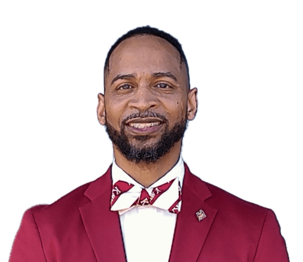 MKYF Man with short hair and beard wearing a maroon suit and a bow tie with white and red stripes, smiling in front of a plain white background.