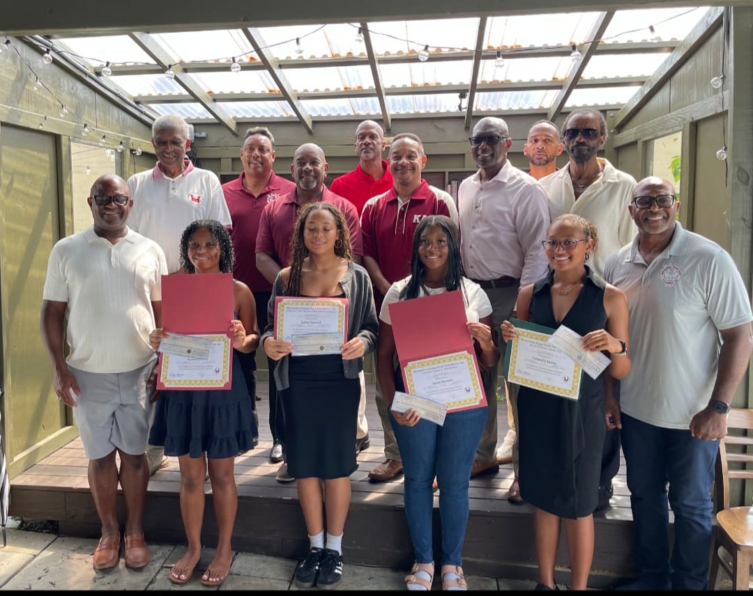 MKYF A group of men and four young women stand indoors; the women in front hold certificates and folders, while the men behind them pose for the photo.